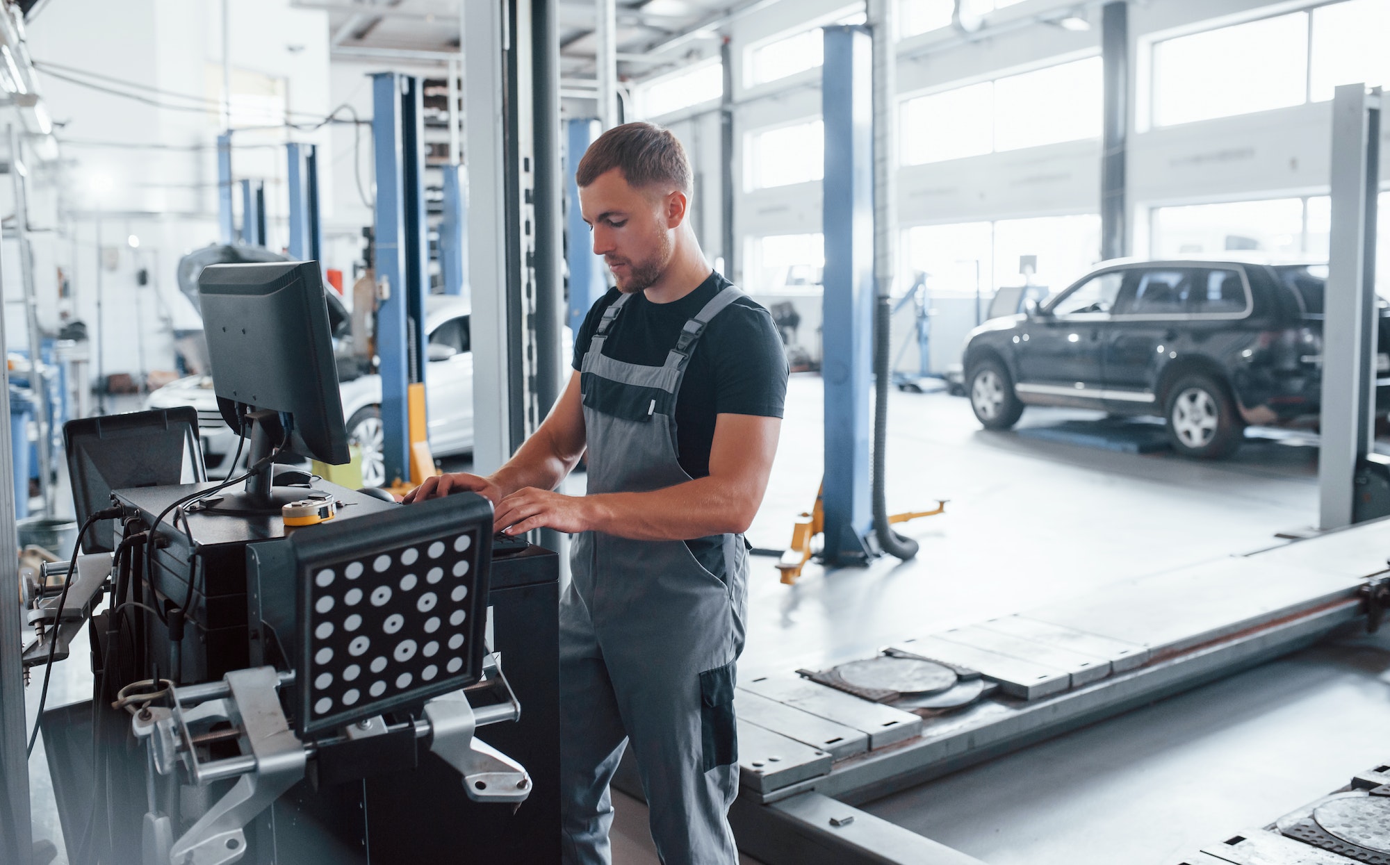 Regarde le clavier. L'homme en uniforme à l'atelier utilise l'ordinateur pour son travail de réparation d'une voiture cassée.