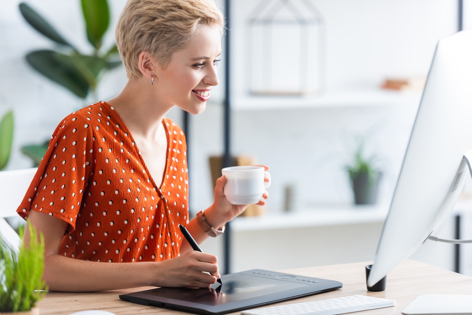 vue de côté d'une travailleuse indépendante heureuse avec une tasse de café dessinant sur une tablette graphique à une table avec