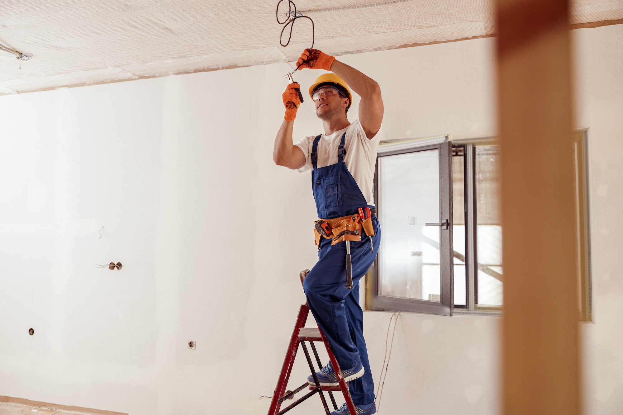 Électricien souriant fixant un câble électrique au plafond