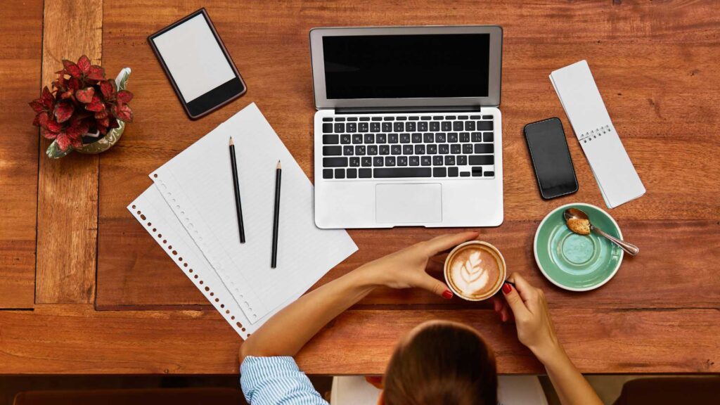 Femme devant son ordinateur avec son café et un bloc-note 