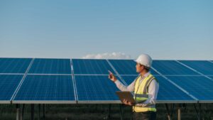 Technicien d’exploitation Energie avec un casque de chantier et un gilet jaune avec son ordinateur dans les mains